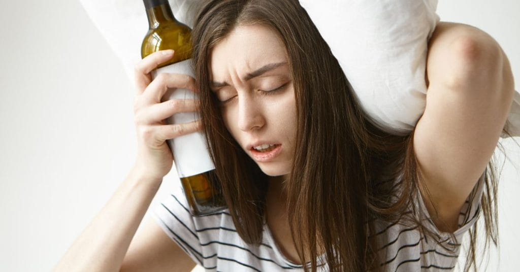 unhappy frustrated young female with messy hairstyle holding a bottle of alcohol